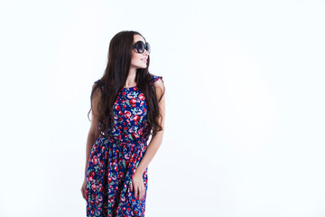Stylish happy woman in dress and sunglasses posing on white wall.