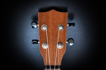 Close up view of a wooden ukulele headstock spotlighted and isolated on a black background.