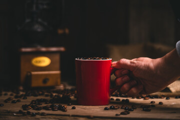 Unrecognizable person with mug of coffee grains at wooden table with manual grinder