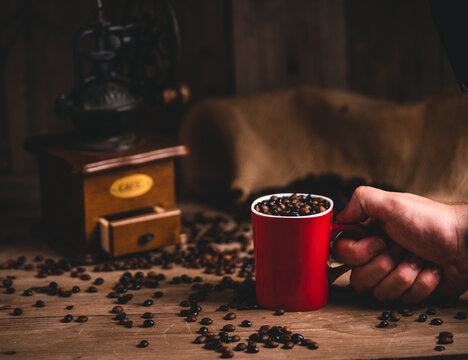 Unrecognizable person with mug of coffee grains at wooden table with manual grinder
