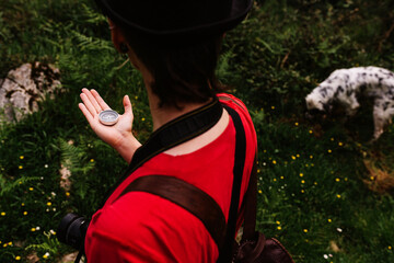 From above back view of female traveler with backpack and photo camera standing on green meadow and orientating by magnetic compass during holiday in Asturias