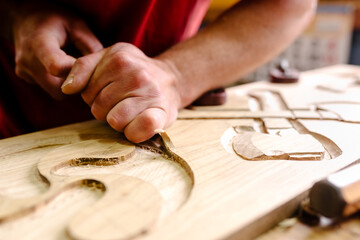 Unrecognizable crop male wood carver using metal chisel while creating ornaments on plank working in workshop