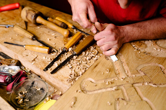 Unrecognizable crop male wood carver using metal chisel while creating ornaments on plank working in workshop