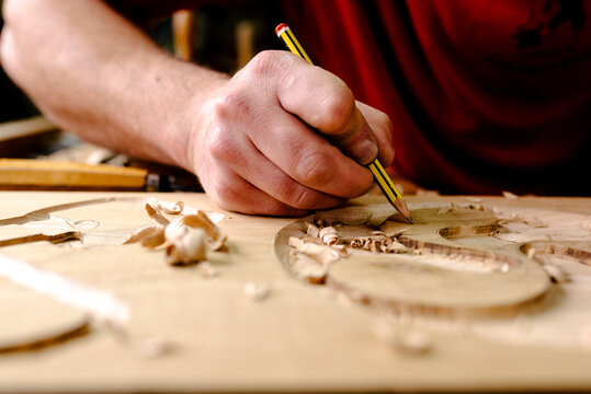 Unrecognizable crop male wood carver using metal chisel while creating ornaments on plank working in workshop