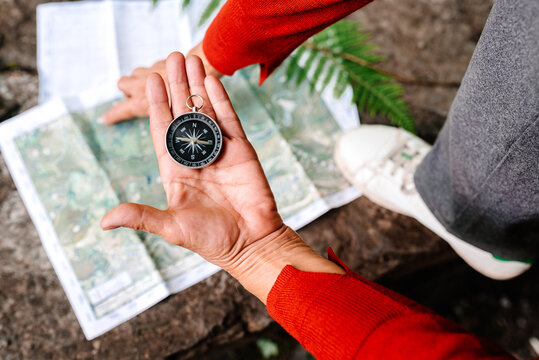 From above of anonymous female tourist orientating on map and compass while standing on rock in forest