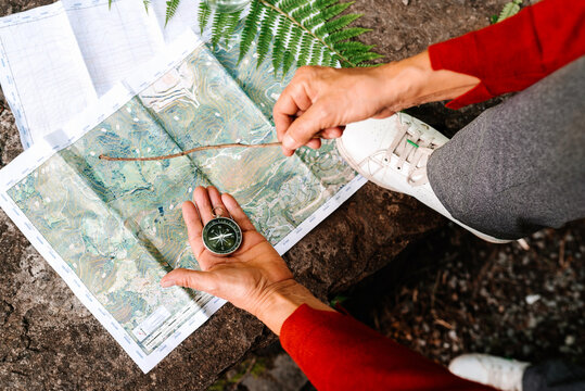 From above of anonymous female tourist orientating on map and compass while standing on rock in forest