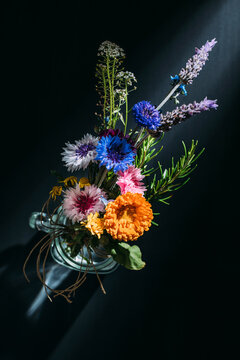 High angle of bouquet of colorful flowers placed in glass cup on black background in studio