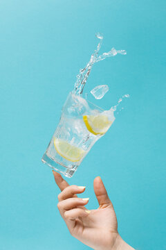 Unrecognizable female tossing glass of fresh water with ice and lemon on light blue background showing concept of diet