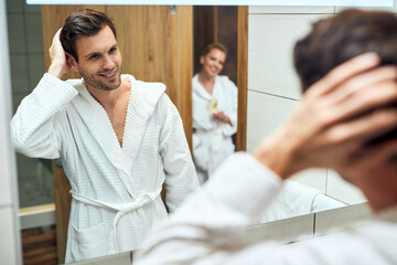 Happy man in bathrobe looking himself in a mirror.