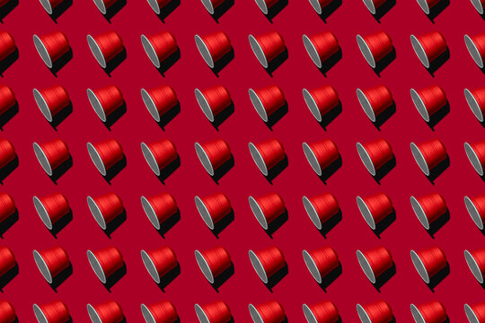 Top view of red coffee pods placed in even rows as seamless pattern on red background