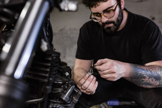 Serious male mechanic repairing dirty spark plug of motorbike while working in garage