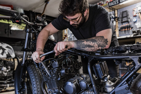 Side view of crop male mechanic using socket wrench and fixing motorbike in workshop