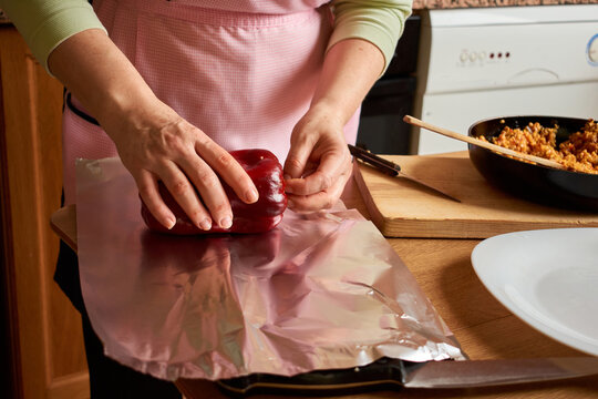 Anonymous housewife wearing apron rolling stuffed pepper in aluminium foil for cooking in oven