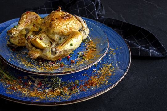 From above of ceramic plates with tasty French coquelet with golden surface garnished with slices of roasted potatoes and seasoned with fresh rosemary and different spices