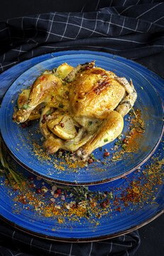 From above of ceramic plates with tasty French coquelet with golden surface garnished with slices of roasted potatoes and seasoned with fresh rosemary and different spices