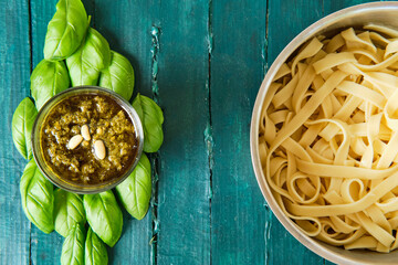 Top view of small glass bowl with famous Italian pesto sauce made of fresh basil leaves and pine nuts covered with olive oil near of delicious Italian pasta