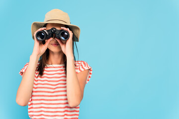  woman in hat looking through binoculars isolated on blue