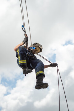 Side view of strong firefighter in protective equipment during training with ropes near building on background of blue sky