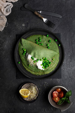 Overhead still life of pea crepes served on a dark dish placed on dark textured board