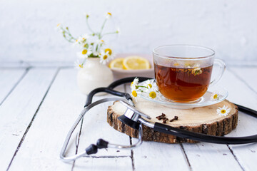 Decoction of chamomile, dried flower in flower tea and a phonendoscope, sliced lemon on a white wooden background. Health concept, prostate treatment, doctor prescribing treatment