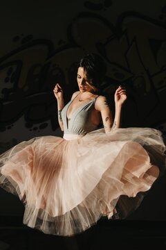 Beautiful young female ballet dancer in translucent tutu performing sensual dance movements in dark studio with eyes closed