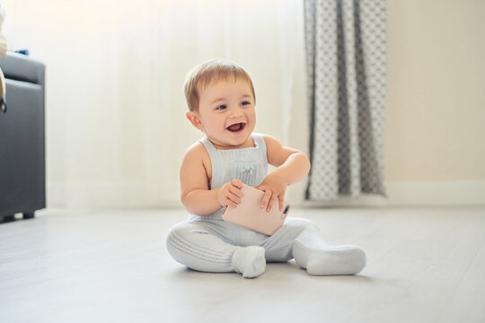Cute excited little toddler with mobile phone in hands sitting on floor in cozy light room at home