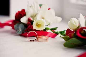 Wedding rings with flowers laying on the white background with red ribbon