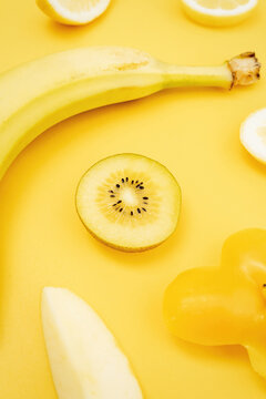 Top view of various fresh fruits and vegetables arranged on yellow background
