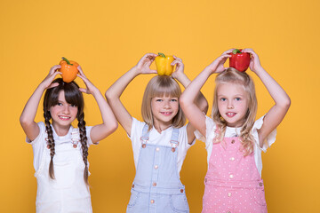 Group of 3 beautiful girls holding in hands yellow, orange, red peppers in background in Studio, looking. Concept of healthy food for children, vegetables, vitamins, nutrients. Schools lifestyle