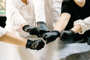 Cropped unrecognizable content cooks team wearing uniform and gloves striking bargain with fists while working in modern restaurant kitchen during coronavirus epidemic