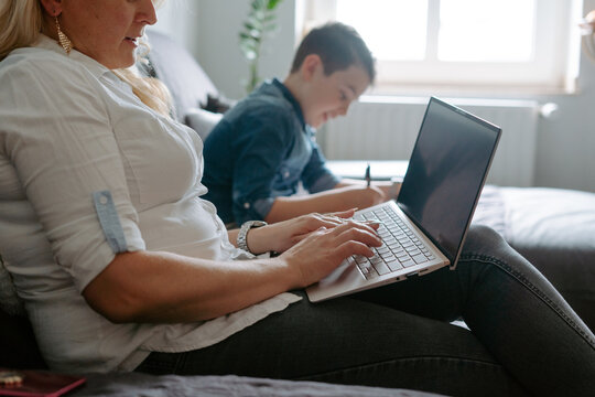 Cropped mother using netbook while sitting near content son with sheet of paper while spending free time together