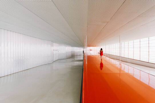 Back view of unrecognizable female standing on shiny orange floor of passage in modern building
