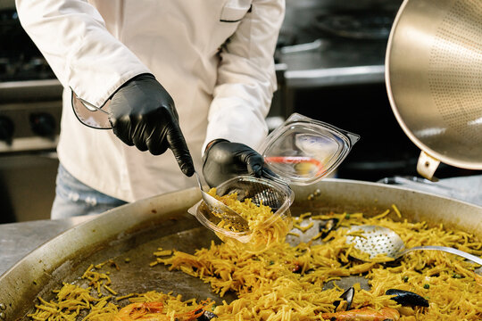 Cropped unrecognizable chef placing delicious noodle with seafood in plastic container for delivery while working in restaurant kitchen