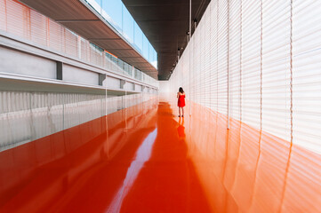 Back view of unrecognizable female standing on shiny orange floor of passage in modern building