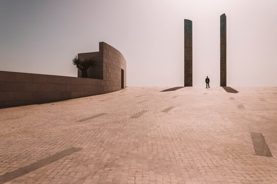 Unrecognizable person standing between stone columns on spacious square near contemporary building of Champalimaud Foundation in Lisbon