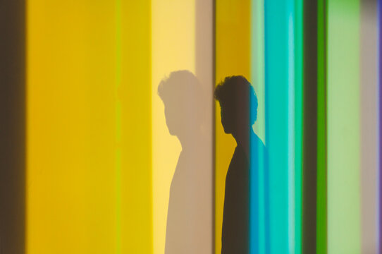 Side view of shadow of young male with curly hair standing in studio with neon lights