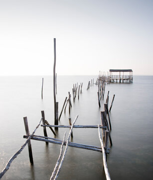 Abandoned partially destroyed dock made of thick wooden sticks on endless ocean with pure water under serene sky in daylight