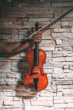 Unrecognizable ethnic male violinist with shiny violin and bow on background of stone wall in modern apartment