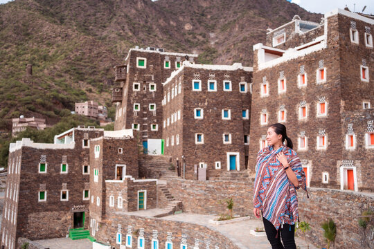 Female tourist standing on background of stone buildings with colorful windows while traveling around Rijal Almaa village in Saudi Arabia