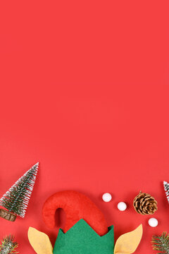 Christmas flat lay with elf hat and ears, snall pine trees and cones and white snowballs at bottom and empty copy space on red background at top