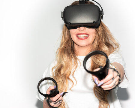 Delighted Female Wearing Goggles Of Virtual Reality Playing Video Game With Controllers While Standing On White Background In Studio