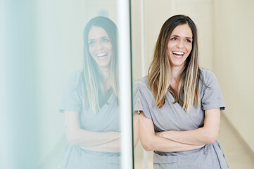 Smiling female professional stomatologist wearing gray uniform holding arms crossed looking away in hospital
