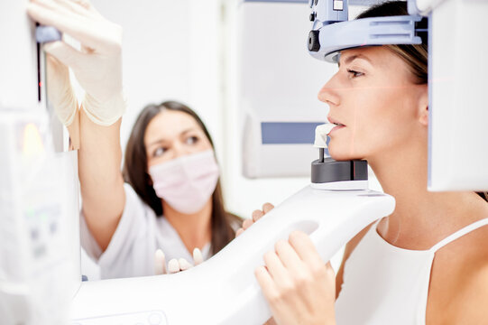 Female dentist using computer while making X ray scan to young woman in contemporary dental clinic