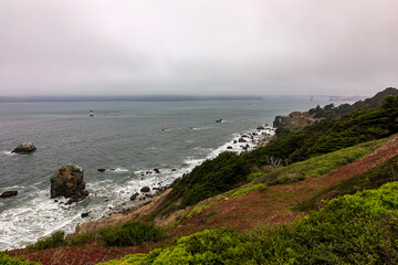 Rugged cliffs and Golden Gate Bridge covered with fog in San Francisco seen from the Lands End trail