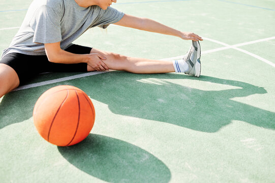 High angle view of young female basketball player sitting on court near ball and doing stretching exercise before game
