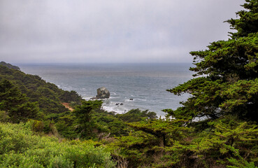 Rugged coastal cliffs and rocks with low fog hanging over the bay seen from the Lands End trail in San Francisco, USA
