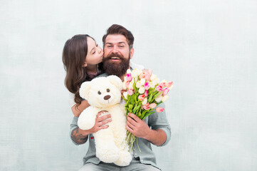 Fototapeta na wymiar Father I love you. Happy daughter kiss father. Bearded man and little child hold flowers and toy. Happy family celebrate holiday. Love and care. Birthday anniversary. Fathers day. Congratulations