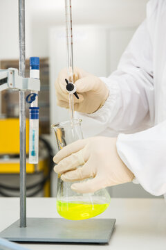 Unrecognizable chemist in protective gloves and uniform standing in laboratory and pouring liquid reagents into flask