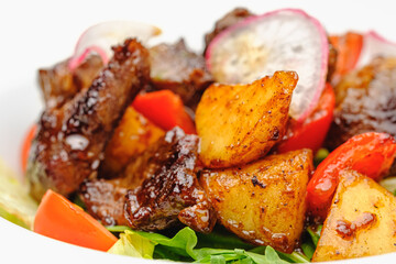 Meat salad with potatoes and grilled vegetables on a white plate.