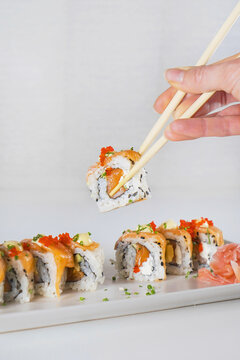From above faceless woman holding sushi with chopsticks above white wooden table